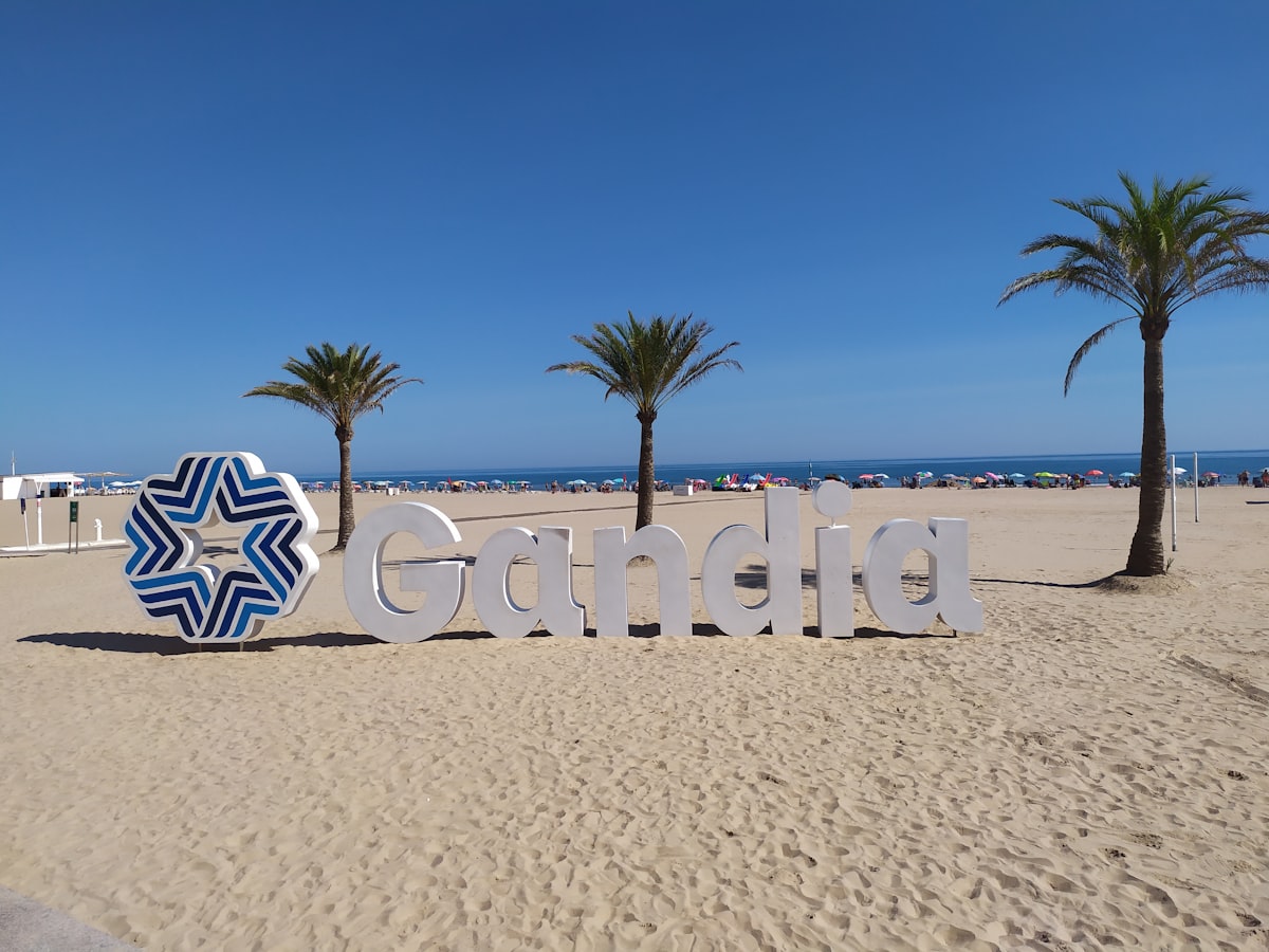 El cartel de Gandia en la amplia playa de arena, con palmeras detrás
